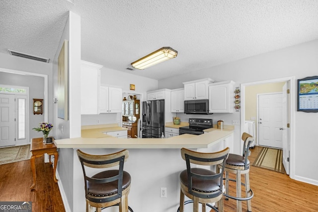kitchen featuring black range with electric stovetop, refrigerator with ice dispenser, stainless steel microwave, light countertops, and light wood-type flooring
