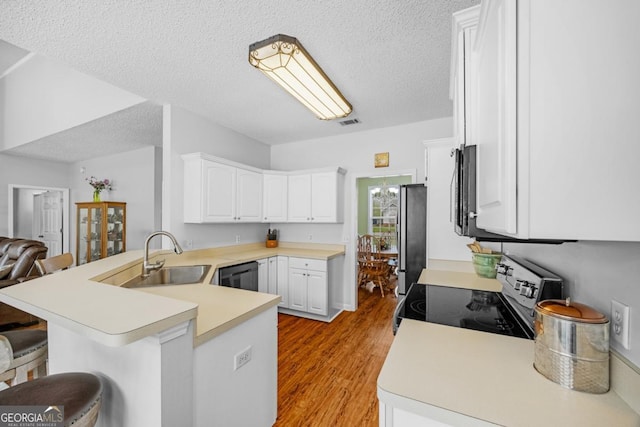kitchen with appliances with stainless steel finishes, a peninsula, a sink, a kitchen bar, and light wood finished floors