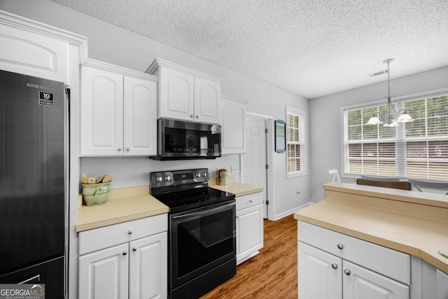 kitchen featuring black electric range, freestanding refrigerator, stainless steel microwave, a textured ceiling, and wood finished floors