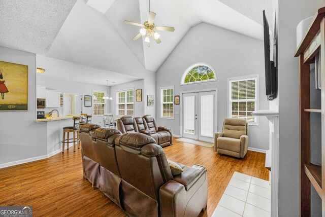living area with a ceiling fan, light wood-style flooring, vaulted ceiling, and baseboards