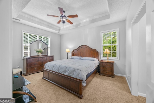bedroom with a tray ceiling, crown molding, a textured ceiling, light colored carpet, and baseboards