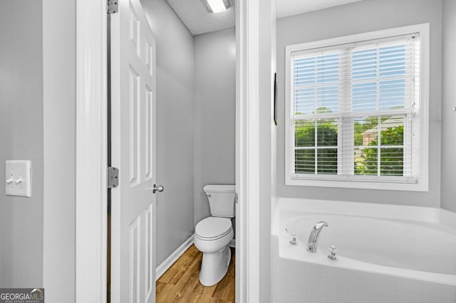 bathroom with a bath, wood finished floors, toilet, and baseboards