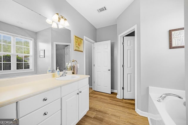 full bath featuring wood finished floors, vanity, a bath, and baseboards