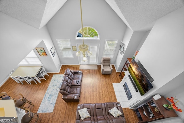 living area with a textured ceiling, baseboards, wood finished floors, and high vaulted ceiling
