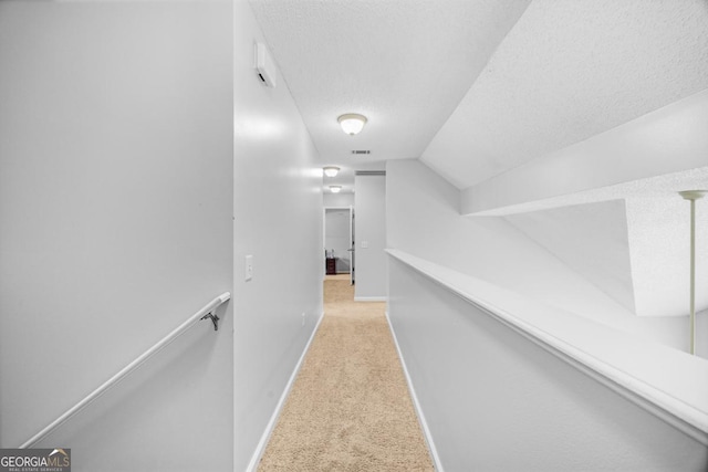 corridor featuring light colored carpet, a textured ceiling, baseboards, vaulted ceiling, and an upstairs landing