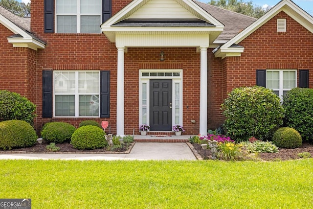 view of exterior entry featuring brick siding and a yard