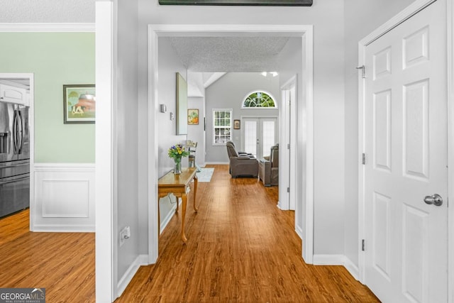 hall with french doors, wood finished floors, wainscoting, a textured ceiling, and baseboards