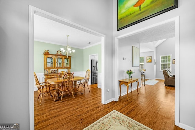 dining space with wood finished floors, a chandelier, crown molding, and baseboards