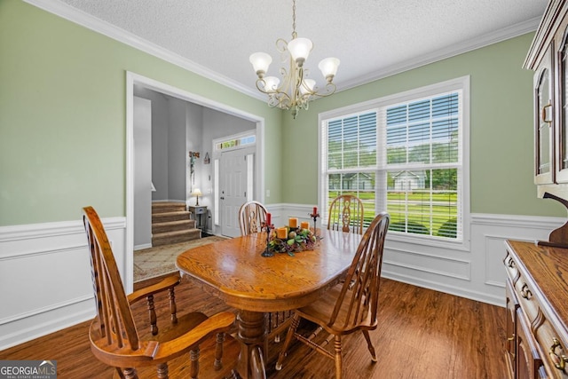 dining room featuring a textured ceiling, a wainscoted wall, a chandelier, ornamental molding, and stairway