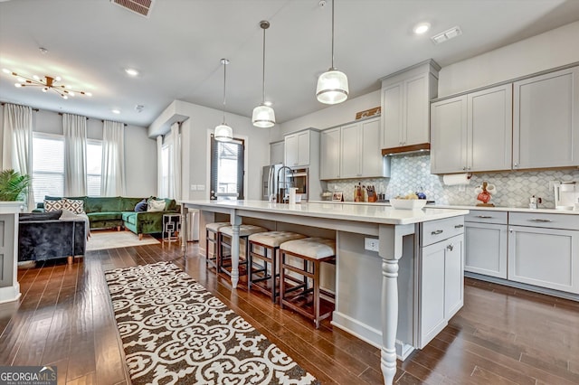 kitchen featuring dark wood-type flooring, a breakfast bar, a spacious island, backsplash, and recessed lighting