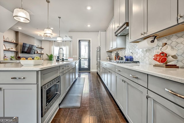 kitchen with a sink, gray cabinetry, appliances with stainless steel finishes, dark wood-style flooring, and backsplash