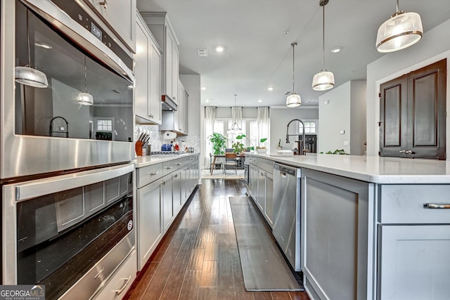 kitchen with a sink, stainless steel appliances, dark wood-type flooring, pendant lighting, and recessed lighting