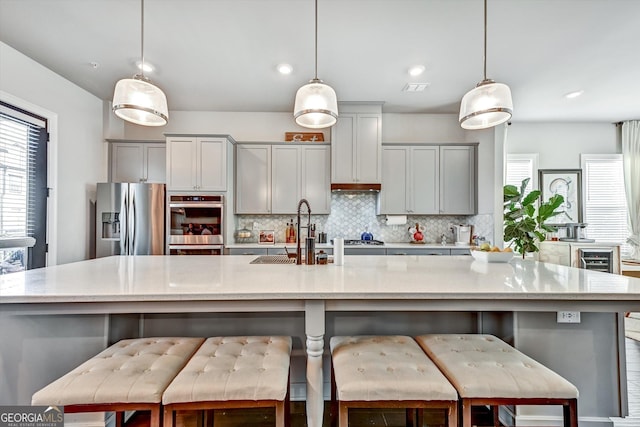 kitchen with stainless steel refrigerator with ice dispenser, a sink, decorative backsplash, a large island, and gray cabinetry