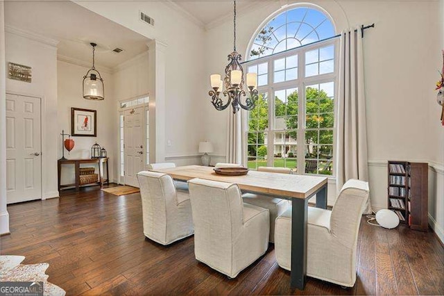 dining area with a chandelier, plenty of natural light, ornamental molding, dark wood-style flooring, and a towering ceiling