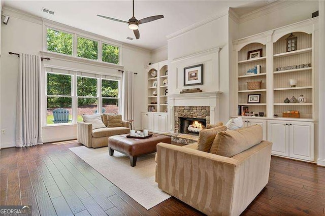 living room featuring crown molding, a ceiling fan, a fireplace, dark wood-style floors, and built in features