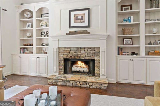 living area featuring dark wood finished floors, a stone fireplace, and built in features
