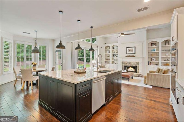 kitchen with stainless steel appliances, a sink, crown molding, ceiling fan, and a stone fireplace