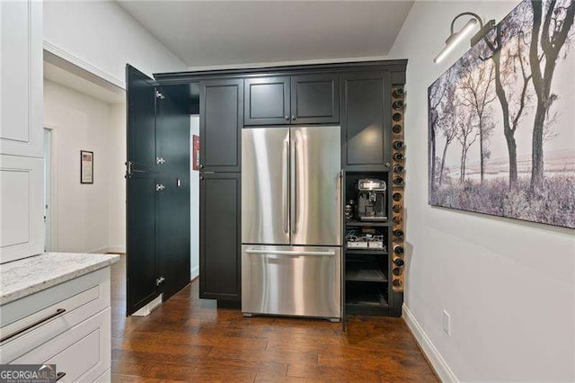 kitchen featuring freestanding refrigerator, dark wood-type flooring, light stone counters, and baseboards