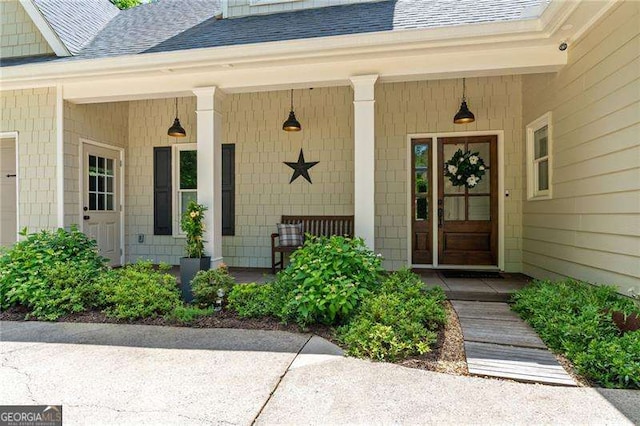 doorway to property featuring roof with shingles and a porch