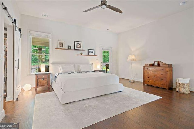 bedroom with a barn door, hardwood / wood-style floors, baseboards, and a ceiling fan
