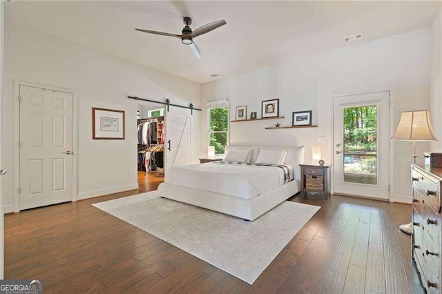 bedroom featuring a barn door, dark wood-type flooring, baseboards, and a walk in closet