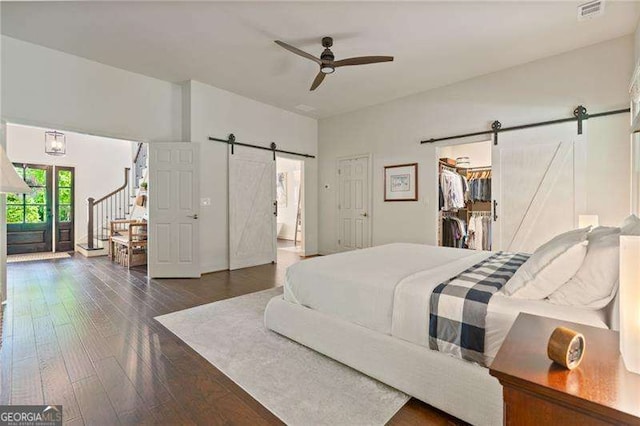 bedroom with a barn door, hardwood / wood-style flooring, a spacious closet, and ceiling fan