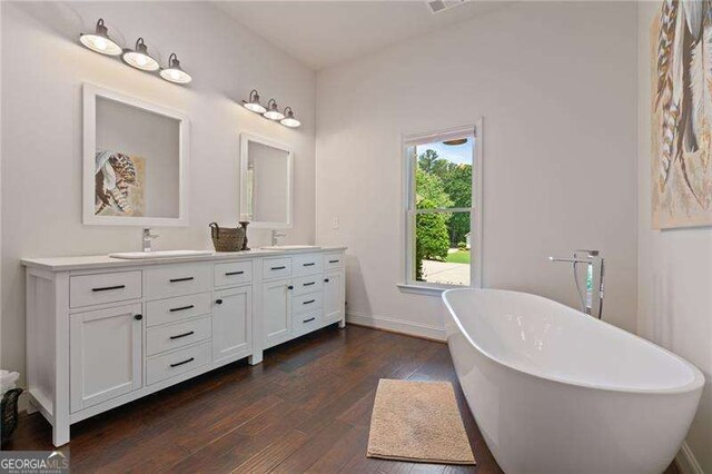 full bath with double vanity, hardwood / wood-style flooring, a soaking tub, and baseboards