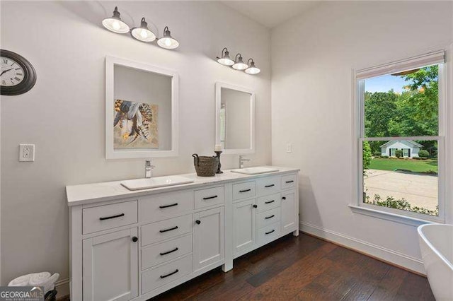 bathroom featuring double vanity, a soaking tub, wood finished floors, and baseboards