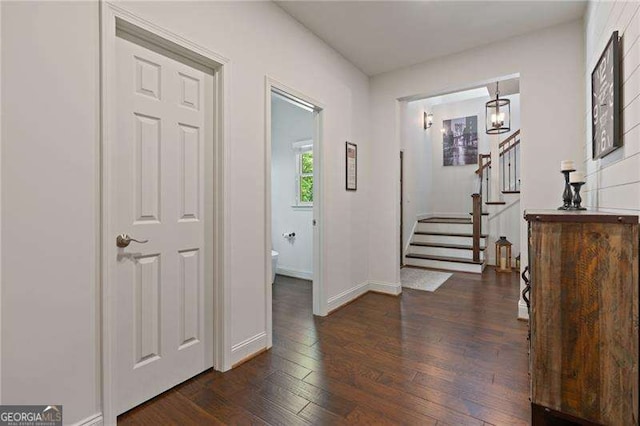 corridor with dark wood finished floors, stairway, baseboards, and a chandelier