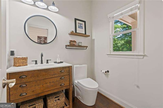 half bath with toilet, vanity, baseboards, and wood finished floors