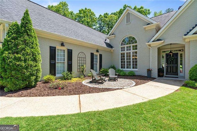 property entrance with brick siding, roof with shingles, and a lawn