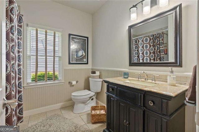bathroom with tile patterned floors, wainscoting, toilet, baseboards, and vanity