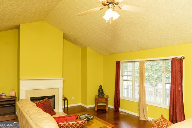 living area featuring a textured ceiling, vaulted ceiling, wood finished floors, ceiling fan, and a fireplace