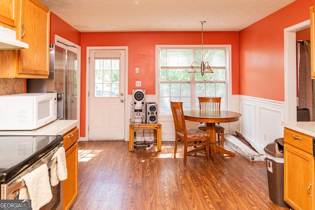 dining space with wood finished floors, a chandelier, wainscoting, a decorative wall, and a textured ceiling
