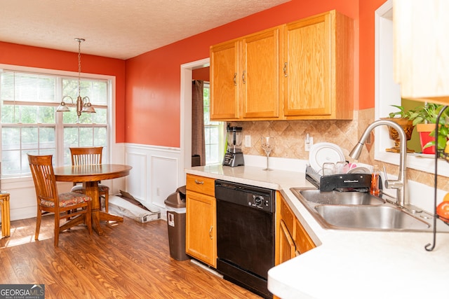 kitchen featuring black dishwasher, a sink, wood finished floors, light countertops, and a wainscoted wall