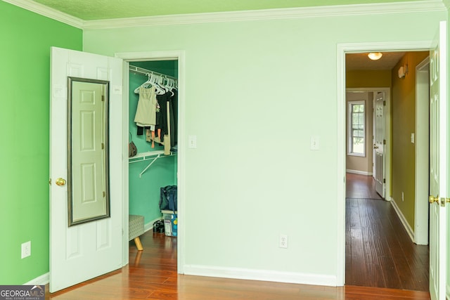 unfurnished bedroom with wood finished floors, a walk in closet, ornamental molding, and baseboards