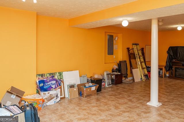 finished below grade area with a textured ceiling, electric panel, and tile patterned flooring