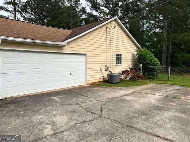 view of property exterior with asphalt driveway, central AC unit, fence, and a shingled roof