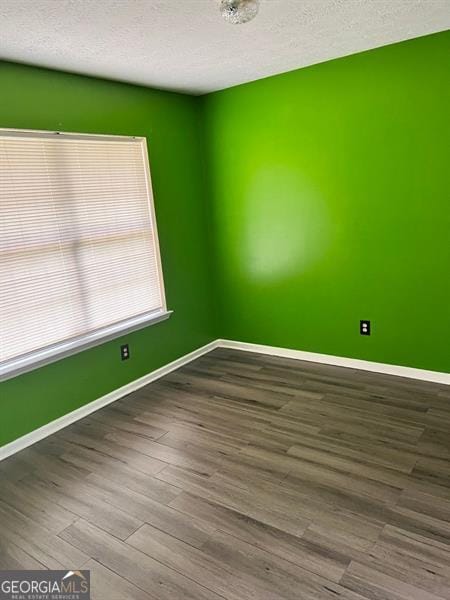 empty room with dark wood-style floors, baseboards, and a textured ceiling