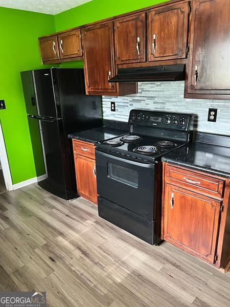 432 Manor Estates Dr, Stockbridge, GA 30281 - kitchen with under cabinet range hood, black appliances, dark countertops, and light wood-style flooring