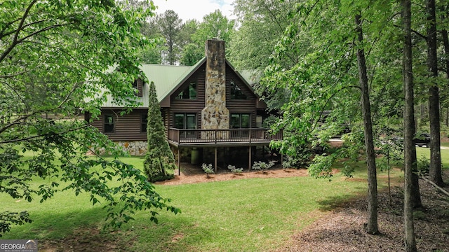 rear view of house featuring a deck, a lawn, a chimney, and log siding