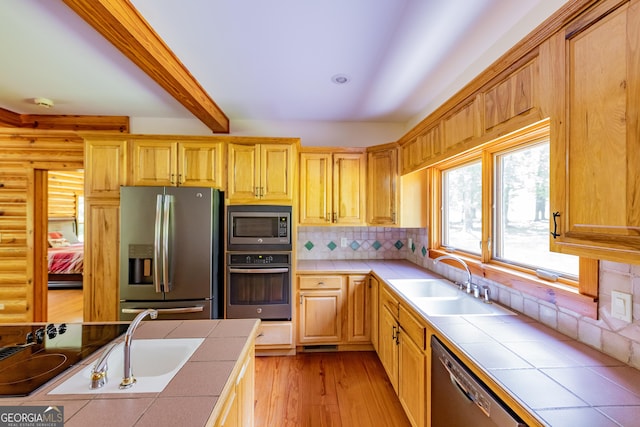 kitchen with appliances with stainless steel finishes, tile countertops, a sink, rustic walls, and beam ceiling