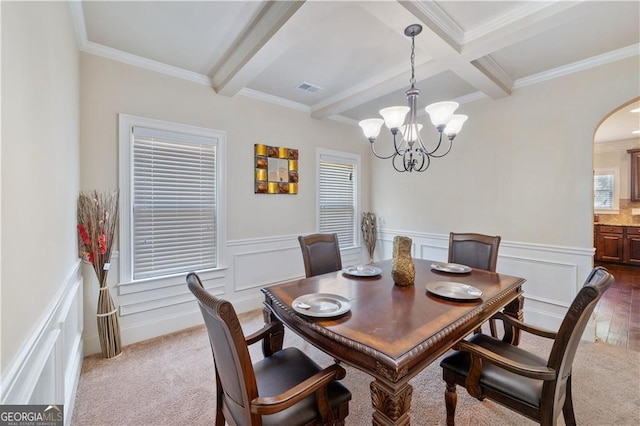 dining space featuring arched walkways, beamed ceiling, a chandelier, ornamental molding, and wainscoting