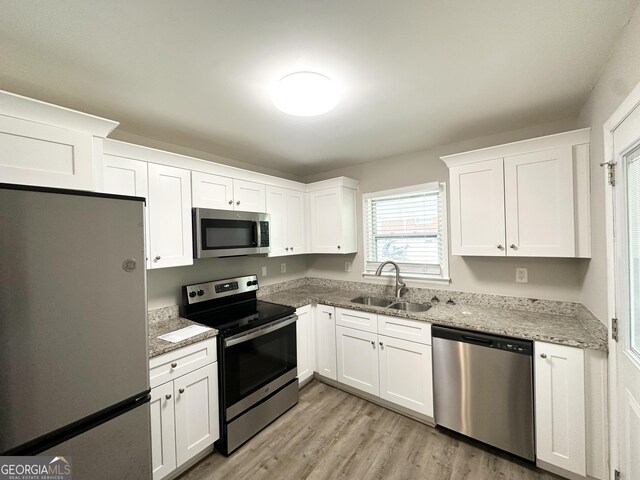 2651 Lois Ln SE, Atlanta, GA 30315 - kitchen with appliances with stainless steel finishes, a sink, white cabinets, light wood-type flooring, and light stone countertops