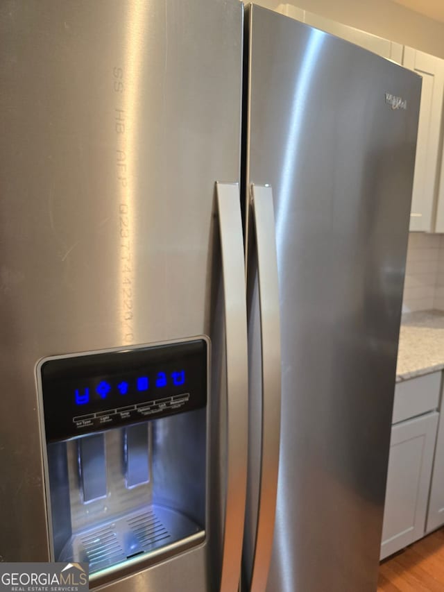 4075 SW Fairburn Ave SW, Atlanta, GA 30331 - detailed view of stainless steel fridge with ice dispenser, light stone counters, light wood-style floors, and white cabinets