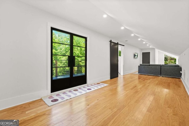 unfurnished living room featuring a barn door, light wood-type flooring, vaulted ceiling, recessed lighting, and baseboards