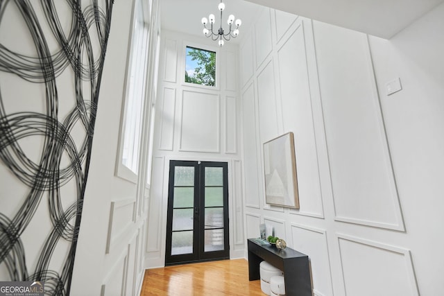 foyer featuring a decorative wall, french doors, a chandelier, and light wood-style flooring