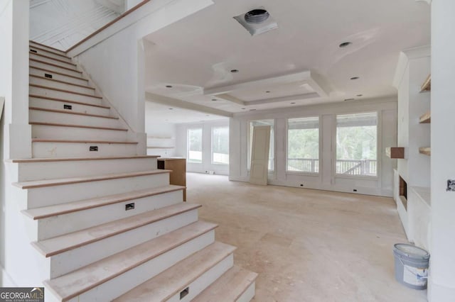 stairs with a fireplace, a tray ceiling, and concrete flooring