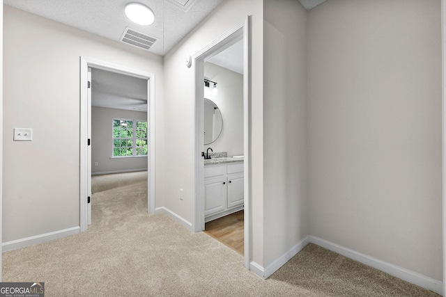 hall with light carpet, baseboards, and a sink