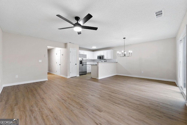 unfurnished living room with a chandelier, a ceiling fan, light wood-style floors, baseboards, and a textured ceiling